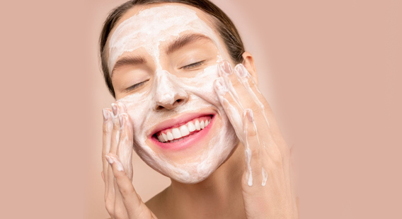 A woman smiling while applying a skincare product on her face 